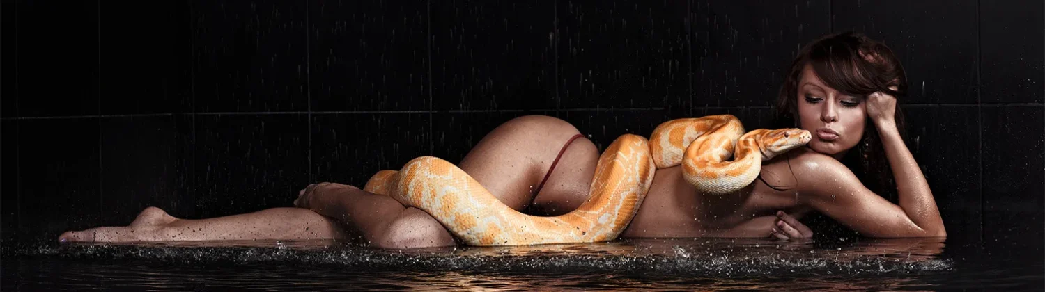 Nude woman posing with a python in a water setting, dramatic lighting.